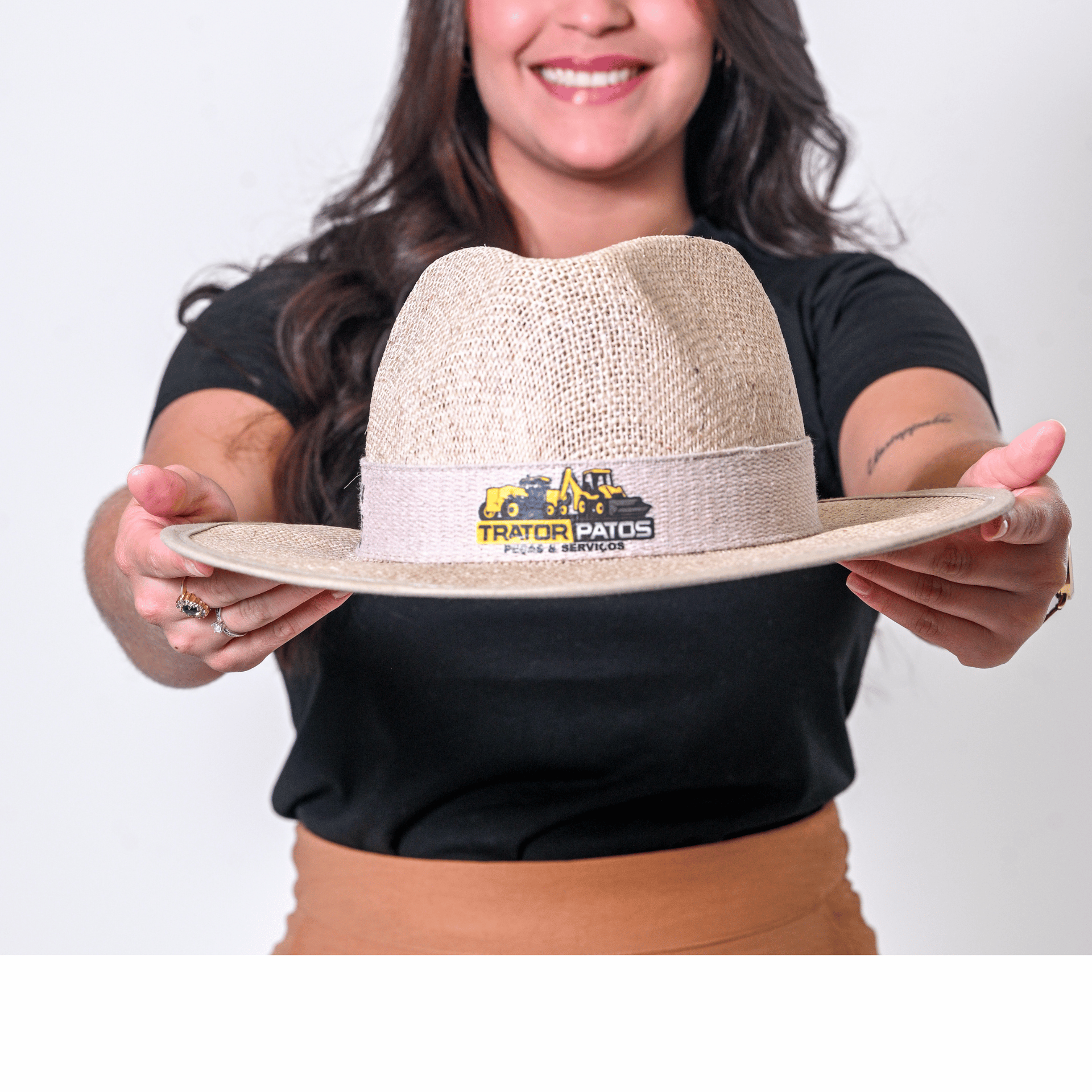 Modelo feminina sorrindo segurando um chapéu de palha de aba média com detalhes na copa.