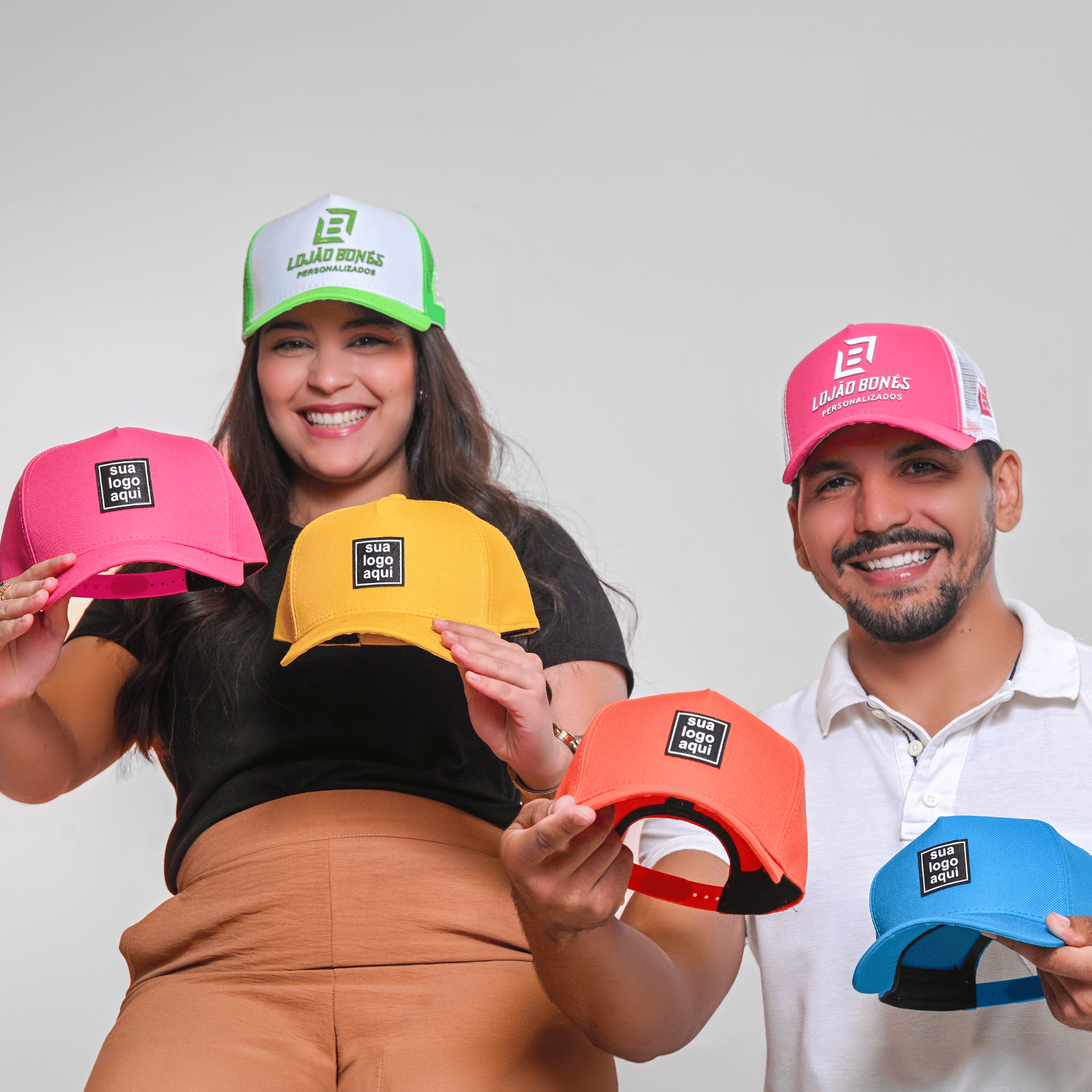 Casal sorrindo usando e segurando bonés de diferentes cores e estilos.