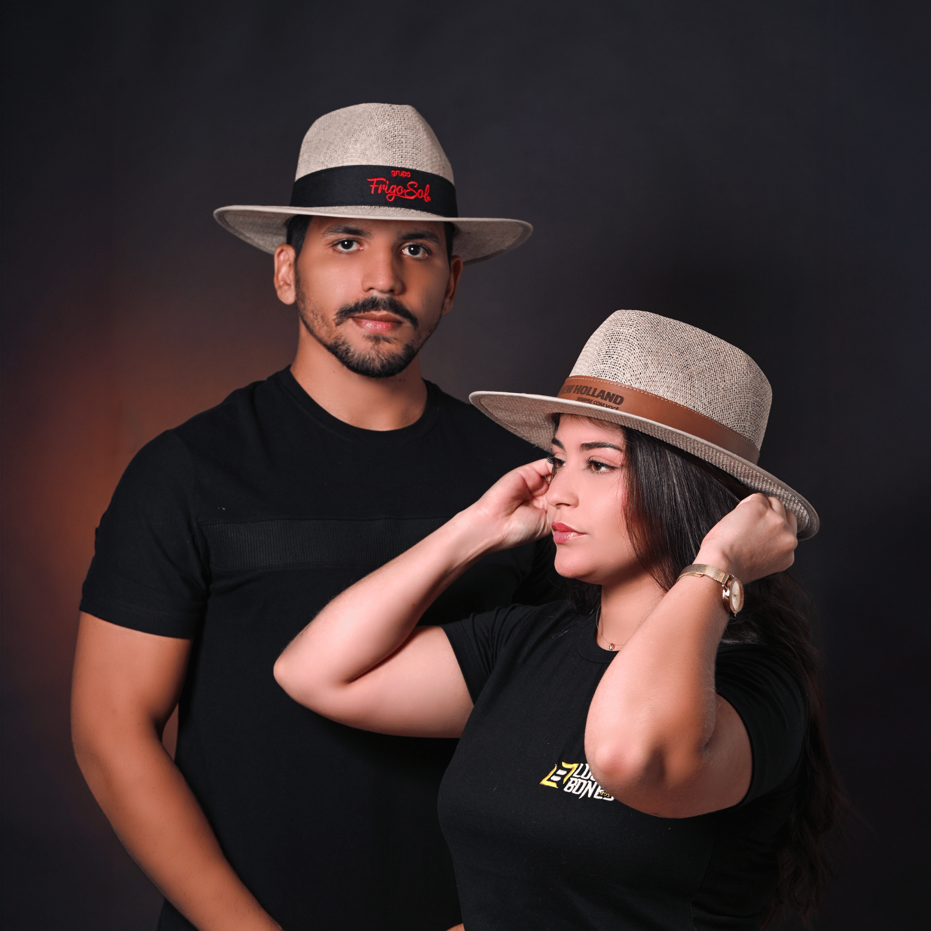 Casal sorrindo usando chapéus de palha de aba curta em ambiente interno.